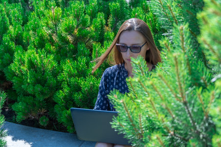 Woman freelance works on laptop in city park. Young adult student education in fresh air. Female...