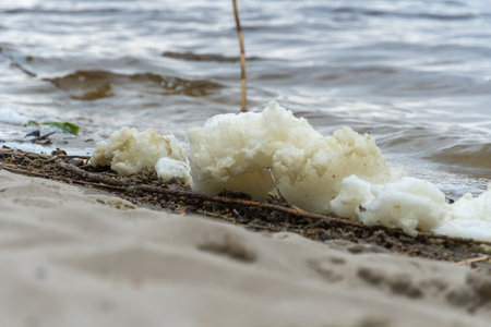 River bank with waves and white foam. White soft foam swaying. Blue water edge on sandy beach. Swirl natural pattern in shallow water.の写真素材