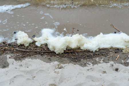 River bank with waves and white foam. White soft foam swaying. Blue water edge on sandy beach. Swirl natural pattern in shallow water. Tranquil scene of beach.の写真素材