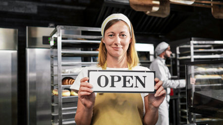 Portrait shot of Caucasian beautiful female baker in apron and hat standing in bakehouse in the...