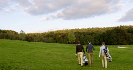 Three male friends with clubs and golf bags walking on the pitch. Golf players coming back from their game. Back viewの写真素材