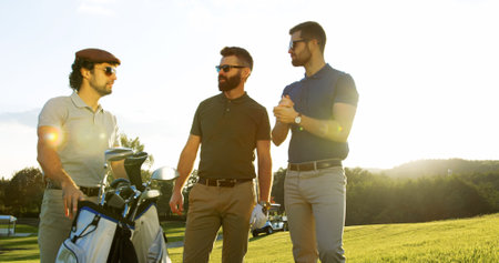 Portrait of three attractive men talking and holding the golf bag on the nice sunny day on the golf pitchの写真素材