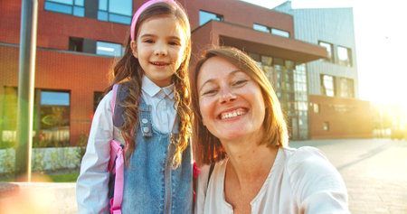 POV of Caucasian happy mother and daughter speaking on webcam while standing outdoor on sunny day. Cheerful woman with cute little schoolgirl video chatting on street. Close up conceptの写真素材