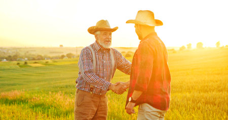 Handshake between the farmers at the field during the examining harvest. Two businessman farmer shake hands. Agree successful deal or hello. Background of agricultural field with growing ripening cornの写真素材