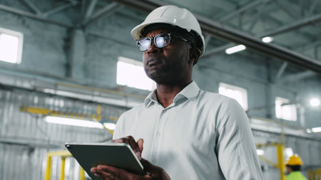 Careful concerned hard-working African-American male wearing white helmet marvelous glasses and...