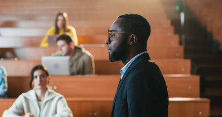 Afican American male professor standing and walking in front of students and giving lection. Man teacher explaining lesson subject in auditorium. Close up. Teaching work. Working at University.の写真素材
