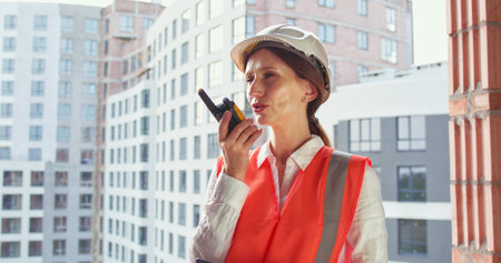 Builder in helmet talking by walkie talkie control and communicate with worker outdoors on construction site at village. Contractor using radio operation in industry.の写真素材