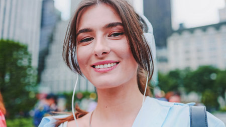 Close up portrait stunning pretty cute caucasian girl walking in big beautiful city wearing headphones listening music and looking to camera.の写真素材