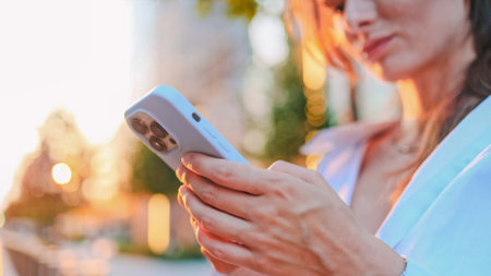 Close up of woman texting, scrolling on smartphone, reading news, searching information in internet outdoors. Background of big city with skyscrapers. Freedom and active lifestyle concept.の写真素材