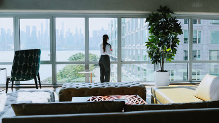 Panoramic view from skyscraper building. Professional businesswoman standing near window in new modern office and talking by smartphone. Communication, management and productive work concept.の写真素材
