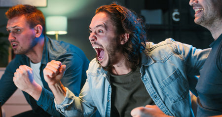 Close up of joyful Caucasian guys sitting on sofa at home late in evening and watching comedy movie...