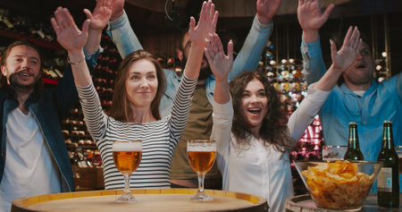 Caucasian male and female friends cheering up in bar when watching sport game. Men and women clapping and doing hands gesture in pub. Football fans watch match on TV with beer and snacks.の写真素材