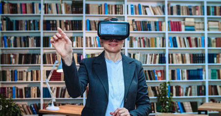 Close-up portrait of scientist wearing virtual reality headset and reading virtual magazine using modern 3D vr glasses in library next to book rack.の写真素材