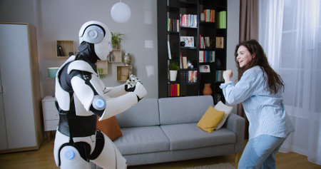 Caucasian woman imitating punches with humanoid cyborg while practicing boxing in living room. Futuristic bionic robot having battle with young lady at home.の写真素材