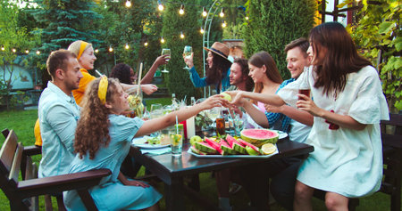 Happy young multi-ethnic people together at garden party. African American and Caucasian girls laughing. Joyful guys and females passing dish while chatting. Pretty Asian girl smiling. Summer conceptの写真素材