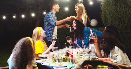 Caucasian boy and girl dancing outdoors. African American and Asian females talking while sitting at...