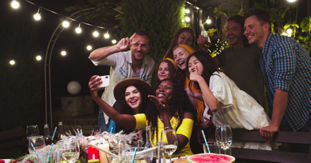 Diverse multi-ethnic young people gathered together at garden party. African American girl sitting...