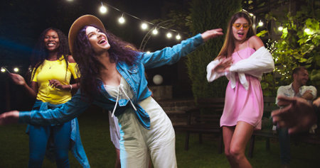 Joyful beautiful mixed-race girls dancing in garden at party. Caucasian and African American females...