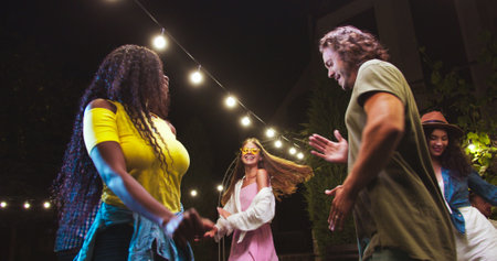 Happy multi-ethnic young people dancing in backyard at party. Portrait of African American girl and Caucasian guy having fun and moving outdoors. Beautiful females and handsome boys dance. Fun conceptの写真素材