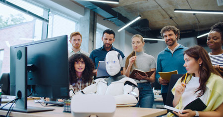 Multi-ethnic colleagues gathering around modern robot. Cyborg sitting at desk with hands on keyboard and moving head from side to side. Team looking confused. Thinking about possible issue.の写真素材
