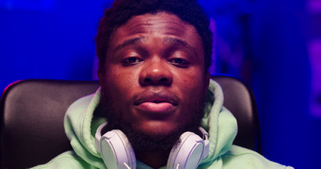 Close up portrait of bearded face African male with headphones on neck. Handsome man sits in room...