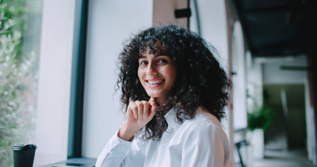 Portrait of Caucasian curly girl looking to camera and smiling. Remote communication. Responding to clients requests. Coworker passing woman.の写真素材