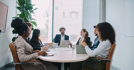Busy director with his managers sitting at round table in modern room with panoramic window. People having business conference. Discussing about ways of company development. Corporate meeting.の写真素材