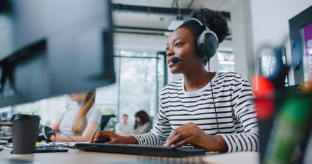 Camera focus on African American woman wearing headset during online consultation with customer. Hardworking manager noting information of conversation on computer. Client service concept.の写真素材
