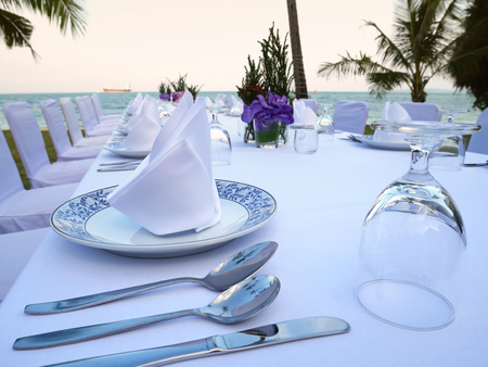 The set of white table and chairs for private dinner party on the beach including napkins, knifes, spoons, glasses and  waiting for the sunset time, romantic time.の写真素材