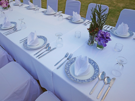 The set of white table and chairs for private dinner party on the beach including napkins, knifes, spoons, glasses and flowers  waiting for the sunset time, romantic time.の写真素材