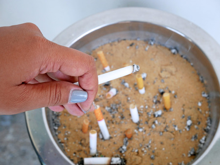 The ashtray of cigarettes allowed at the public place with lady' hand.の写真素材