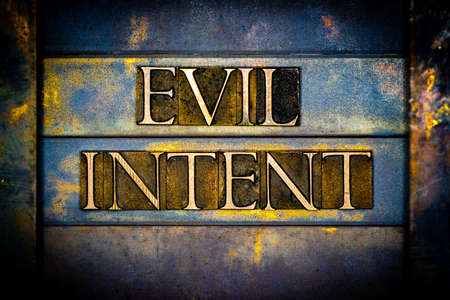 Evil Intent text formed with real authentic typeset letters on vintage textured silver grunge copper and gold backgroundの写真素材