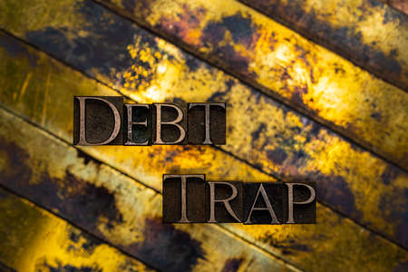 Debt Trap text formed with real authentic typeset letters on vintage textured silver grunge copper and gold backgroundの写真素材