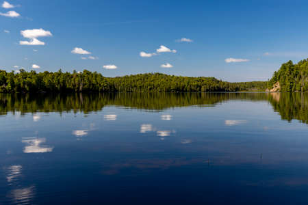 Serene Canadian lake landscape with white cloud reflections and blue skyの写真素材