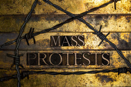 Mass Protests text message on textured grunge copper and vintage gold background bordered by barbed...