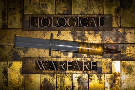 Biological Warfare text with fluid filled syringe on grunge textured copper and gold backgroundの写真素材