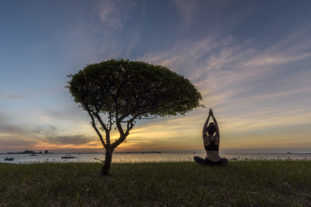 Silhouette young woman practicing yoga on the beach at sunset.