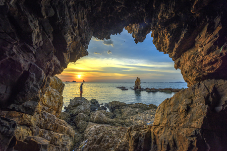 Man looking Rock standing alone, view from cave at sunsetの写真素材