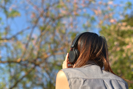 girl turn back listening music under tree flowers in backgroundの写真素材