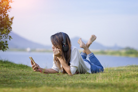 girl enjoy listening music on the grass field of the park in the morningの写真素材