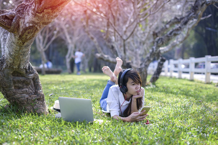 Woman enjoy listening music on line under tree on the grass in park at morningの写真素材