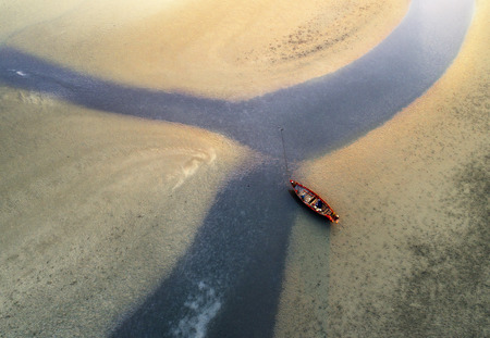 small fishing boat waiting hight tide on the channel of sand beach, aerial viewの写真素材