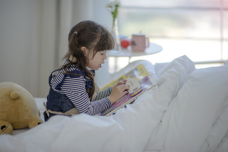 kid girl reading a toy book on the bedの写真素材