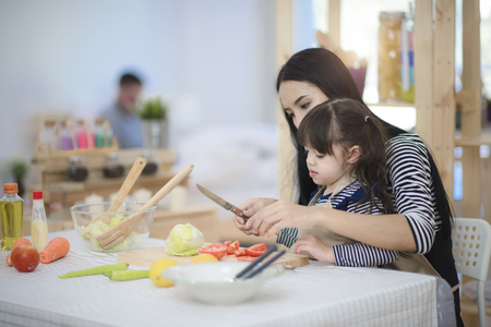 family of kid girl and mom cooking salad practice together in the kitchenの写真素材