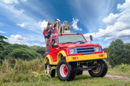 woman in group are enjoy traveling by standing on the rack-back of the convertible car in jungle backgroundの写真素材