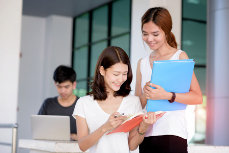 group of students are in attending of tutorial by standing and reading books in hands with University building and other student working in backgroundの写真素材