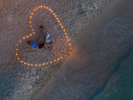 Top view of couple lover in romantic honeymoon by laying on the sea beach in lighting signs of heart, valentine day occasionの写真素材