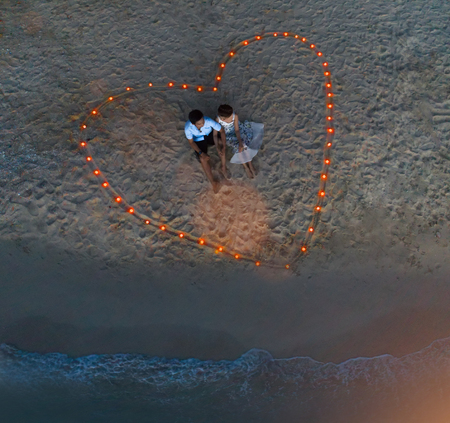 Top view of couple lover in romantic honeymoon by sitting together on the sea beach in lighting signs of heart, valentine day occasionの写真素材