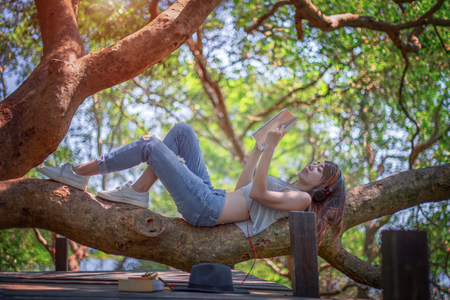 woman easy reading and listening music on the branch of tree over the wooden bridge in the rainforestの写真素材