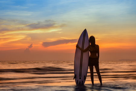 woman holding a surfboard in hand laying on back beside, on returning home station after played surf in the sea at sunsetの写真素材